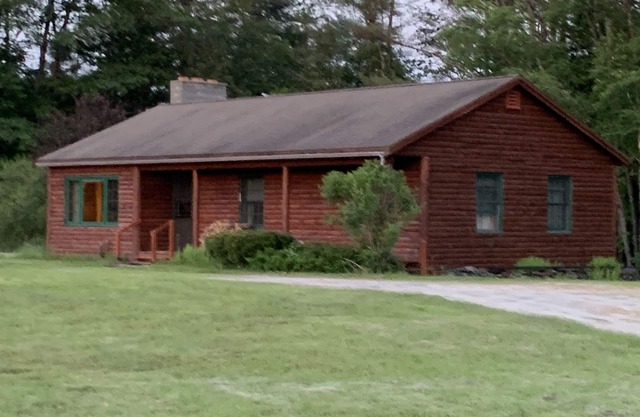 Cabin is nestled near the Sugar River in a country setting next to a open field.